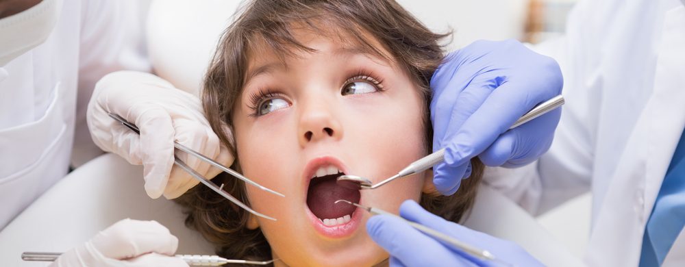 Pediatric dentist examining a little boys teeth with his assistant  at the dental clinic